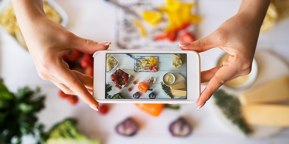 hands holding a phone taking a photo of vegetables